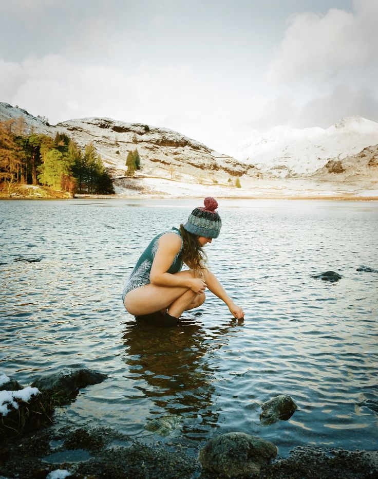 a woman kneeling down in the water with her legs crossed and wearing a beanie