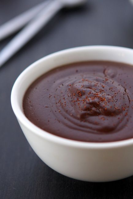 a white bowl filled with chocolate pudding on top of a black tablecloth next to a spoon