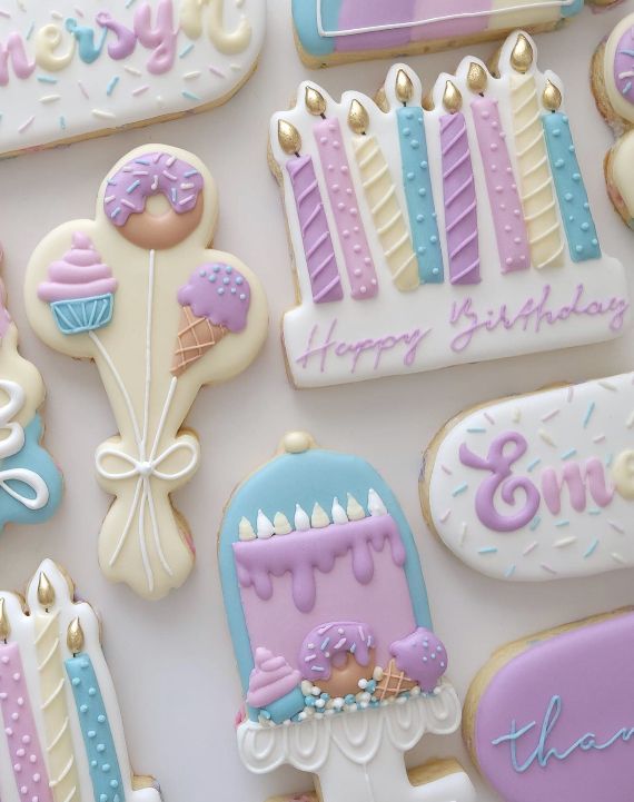 decorated cookies with candles and frosting are displayed on a white tablecloth that says happy birthday