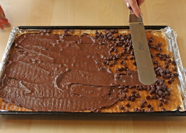 a person is cutting into a chocolate cake on a pan with frosting and chocolate chips