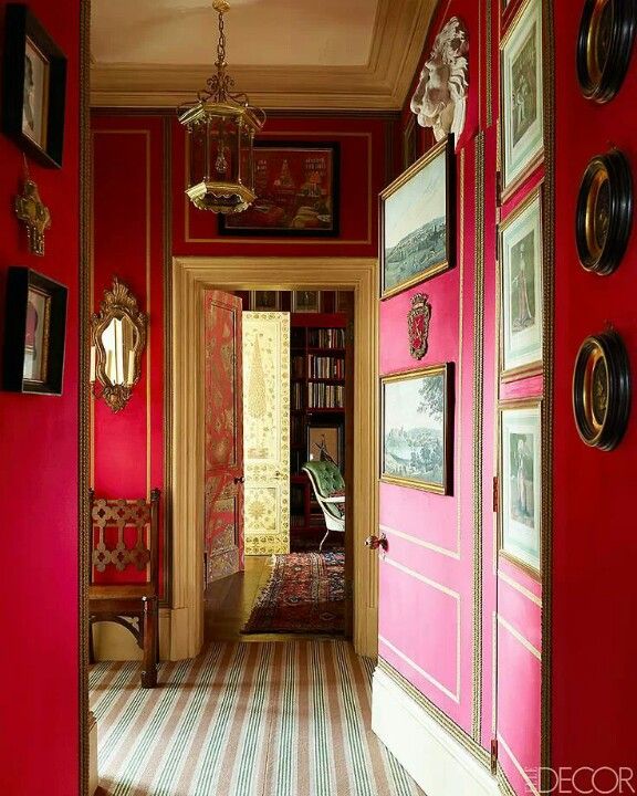 the hallway is painted bright red and has pictures on the walls, along with a chandelier