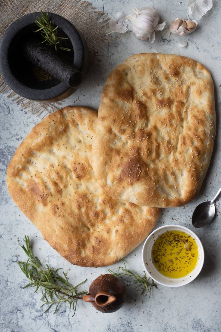 two pita breads sitting on top of a table next to garlic and olive oil