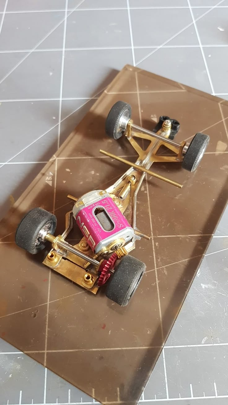 a toy car sitting on top of a brown piece of cardboard with metal parts attached to it