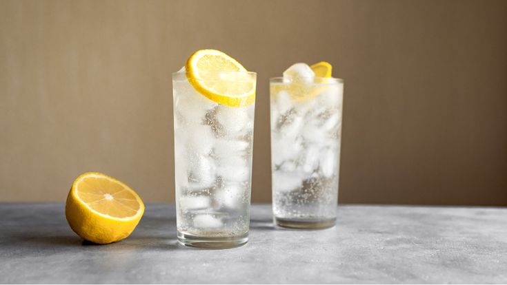 two glasses filled with ice and lemons next to each other on a counter top