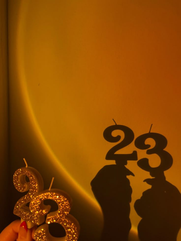 the shadow of two people holding candles in front of a wall with numbers on it