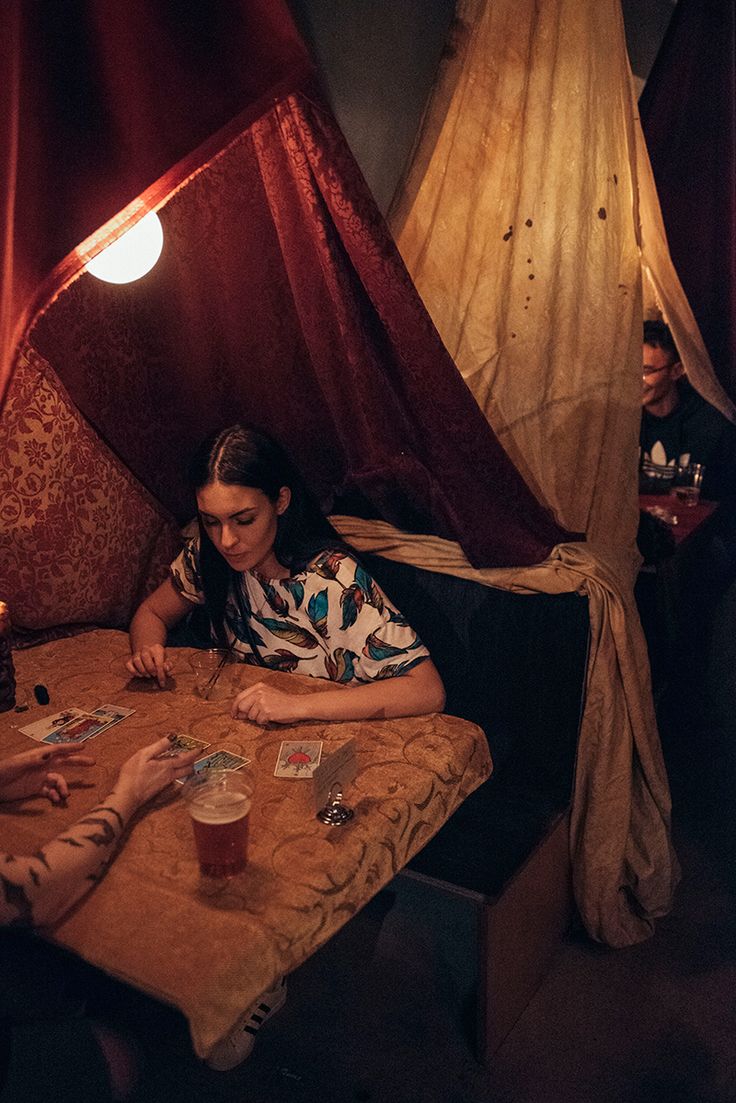 two people sitting at a table playing cards in a room with red drapes on the walls