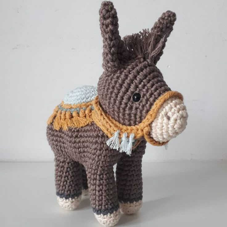 a crocheted donkey is standing on a white surface and wearing a brown scarf