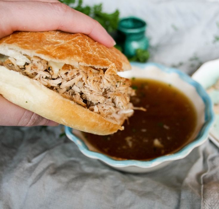 a person is holding a sandwich over a bowl of chili and meat sauce on a table