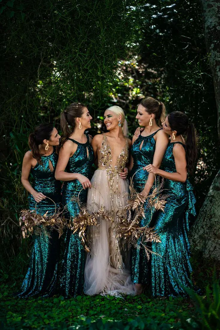 four women in green and gold gowns standing next to each other with trees behind them