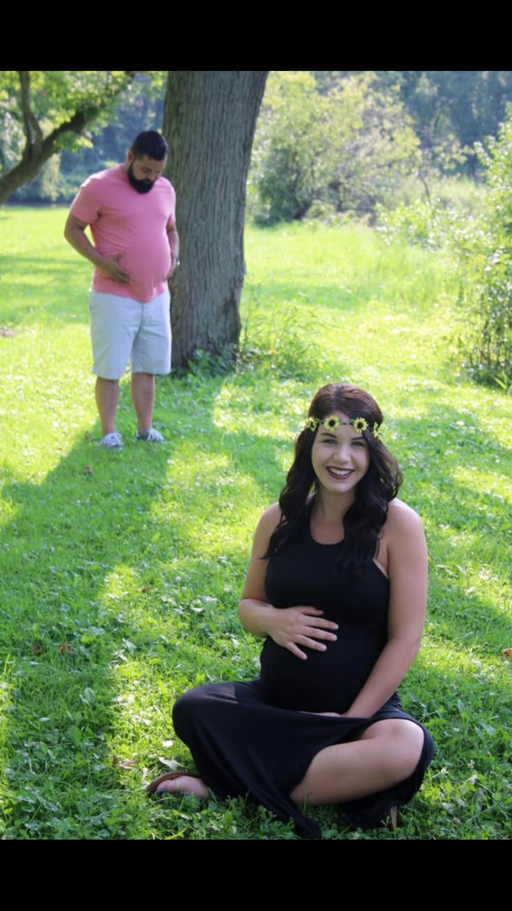 a pregnant woman sitting in the grass next to a man