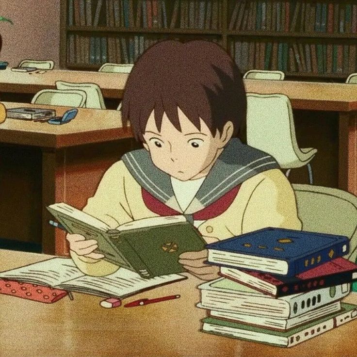 a young boy sitting at a table reading a book in front of bookshelves