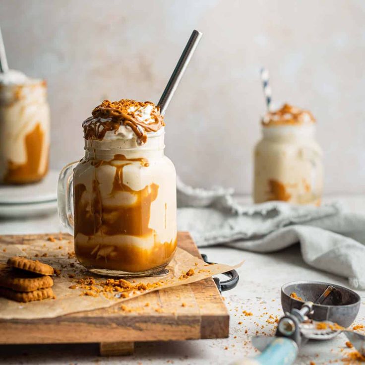 two glasses filled with ice cream and caramel on top of a wooden cutting board