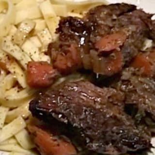 some meat and pasta on a plate with broccoli in the backgroud