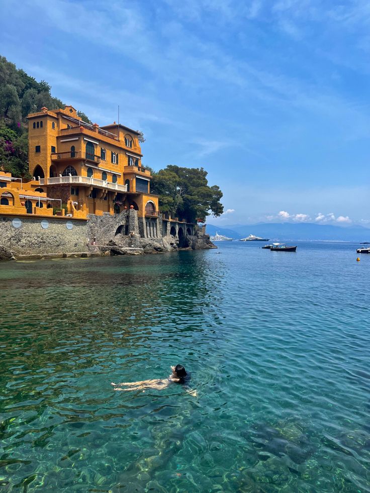 a person swimming in the ocean next to a large yellow building with several balconies