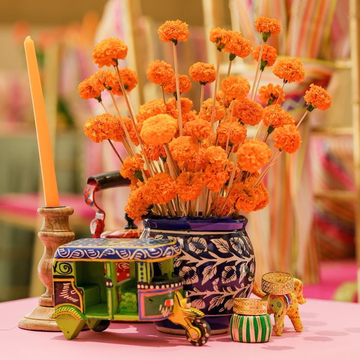 an arrangement of orange flowers in a vase on a pink table cloth with other decorations