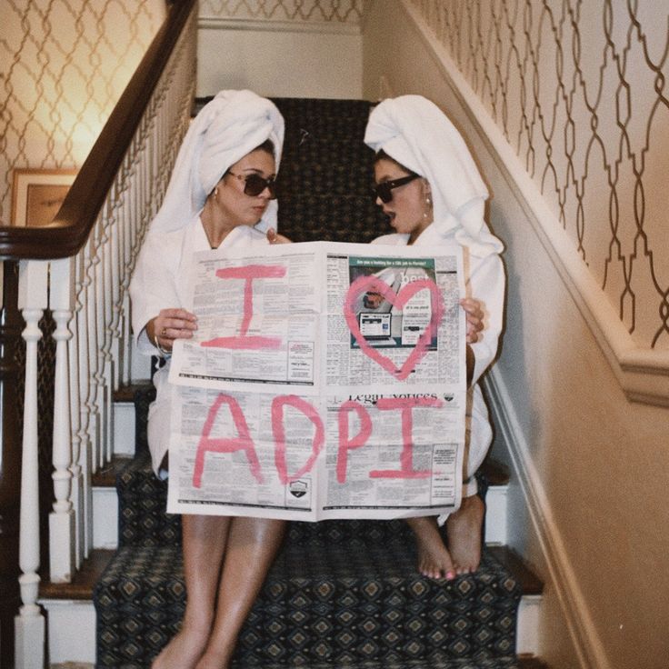 two women sitting on the stairs holding up a newspaper with i love apple written on it