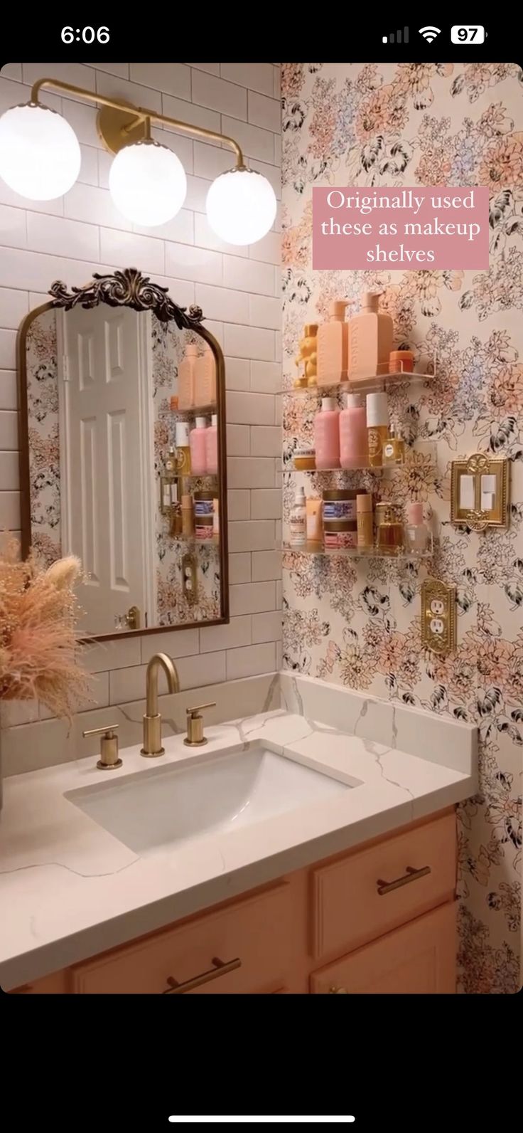 a bathroom with floral wallpaper and gold faucet lights on the vanity mirror