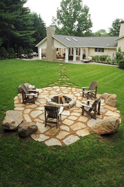 a stone fire pit in the middle of a yard with chairs and tables around it