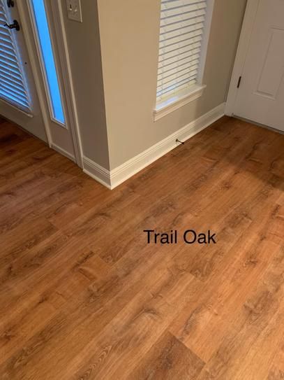 an empty room with wood flooring and white shutters on the door, which reads trail oak