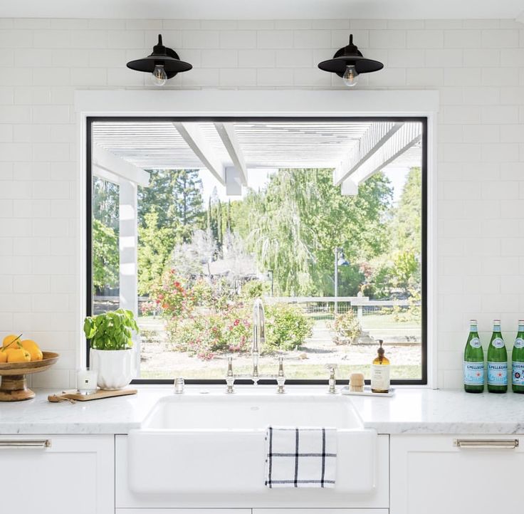 a kitchen with an open window and white counter tops, along with bottles on the counters