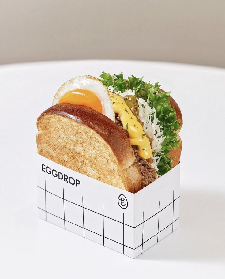 a close up of a sandwich in a box on a white surface with an egg and cheese