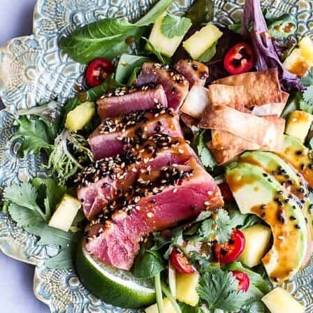 a salad with tuna, avocado, and tomatoes on a blue plate topped with sesame seeds