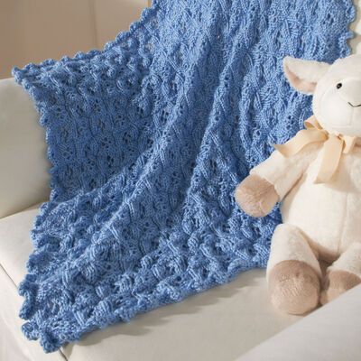 a teddy bear is sitting on a couch next to a crocheted baby blanket