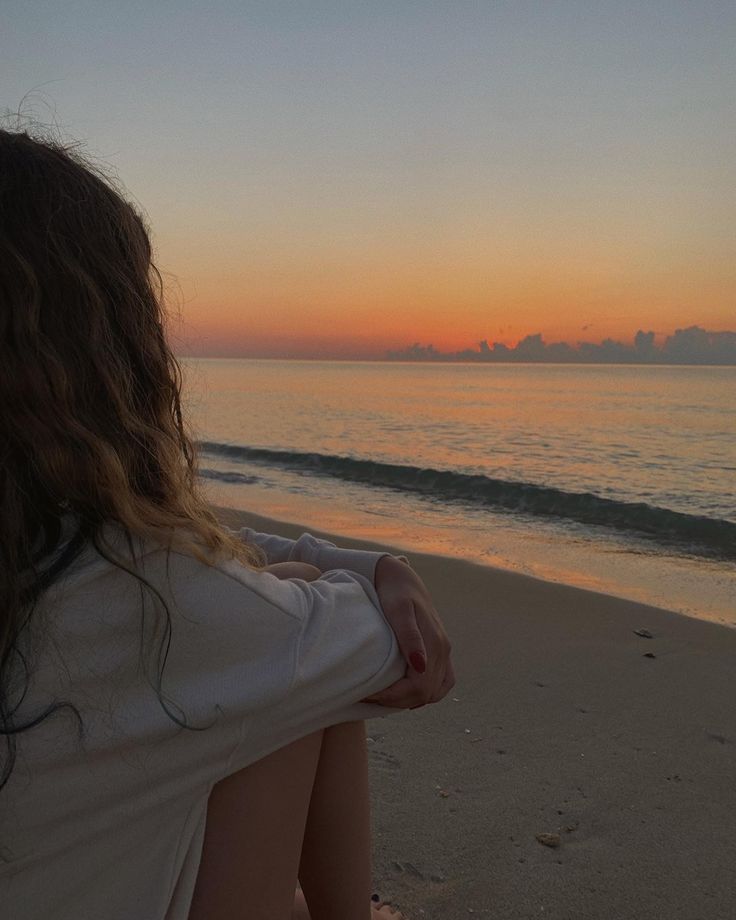 a woman sitting on the beach watching the sunset