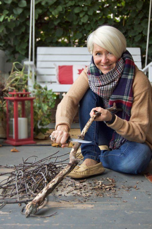 a woman sitting on the ground holding a pair of scissors next to twigs and branches