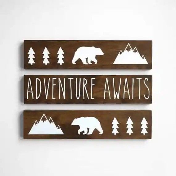 three wooden signs with the words adventure awaits and an image of a bear, tree, and mountain