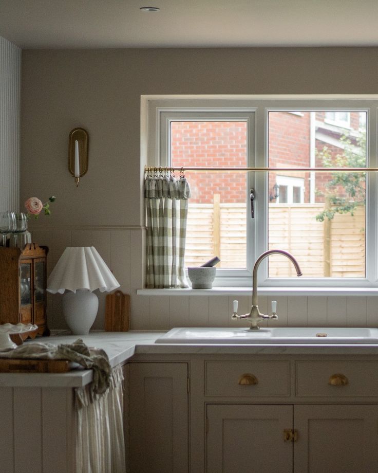 a kitchen sink sitting under a window next to a lamp