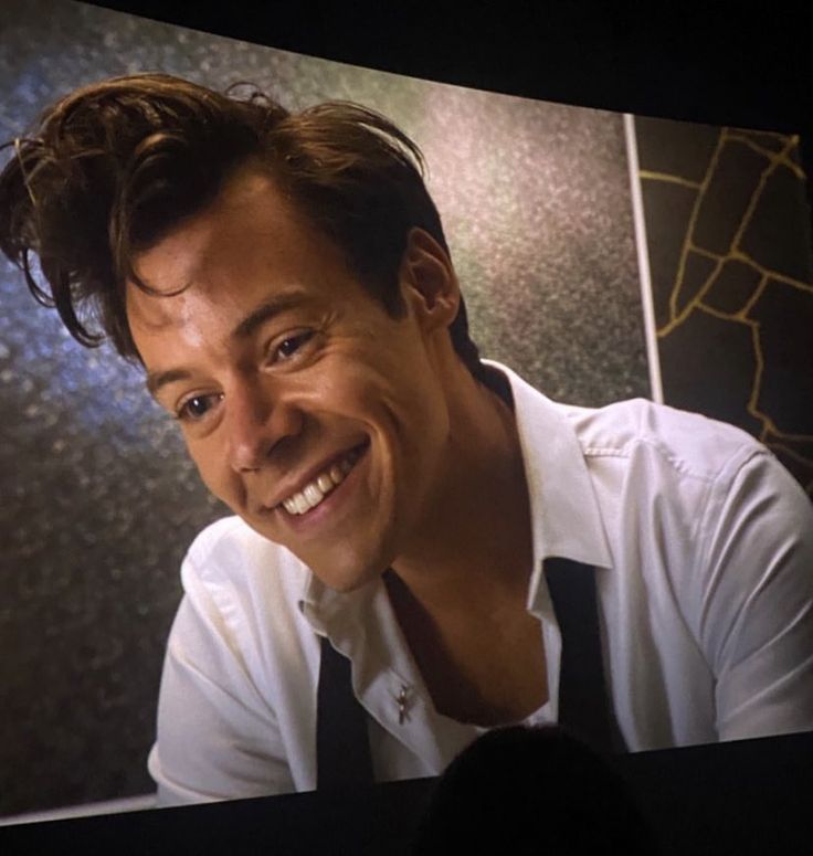 a man smiling while wearing a white shirt and black tie in front of a tv screen