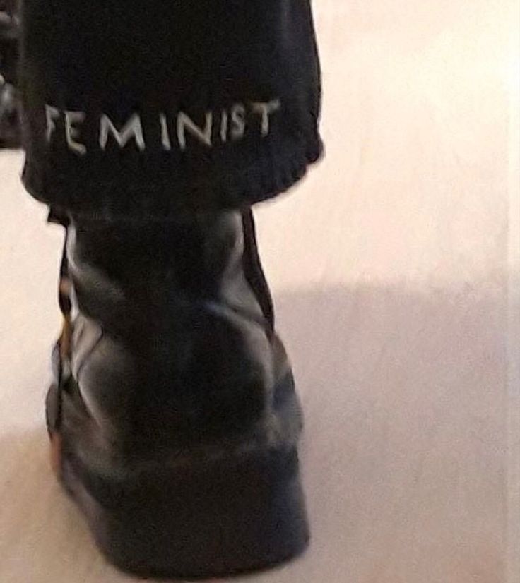 a person wearing black boots with the word feminist written on it's soles