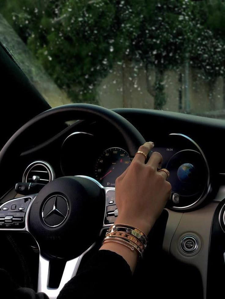 a person driving a car in the rain with their hand on the steering wheel and dashboard