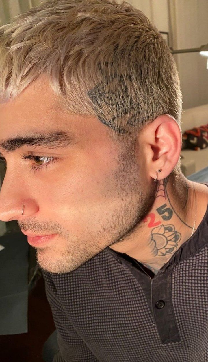 a man with tattoos on his neck looking at something in the distance while wearing a brown shirt