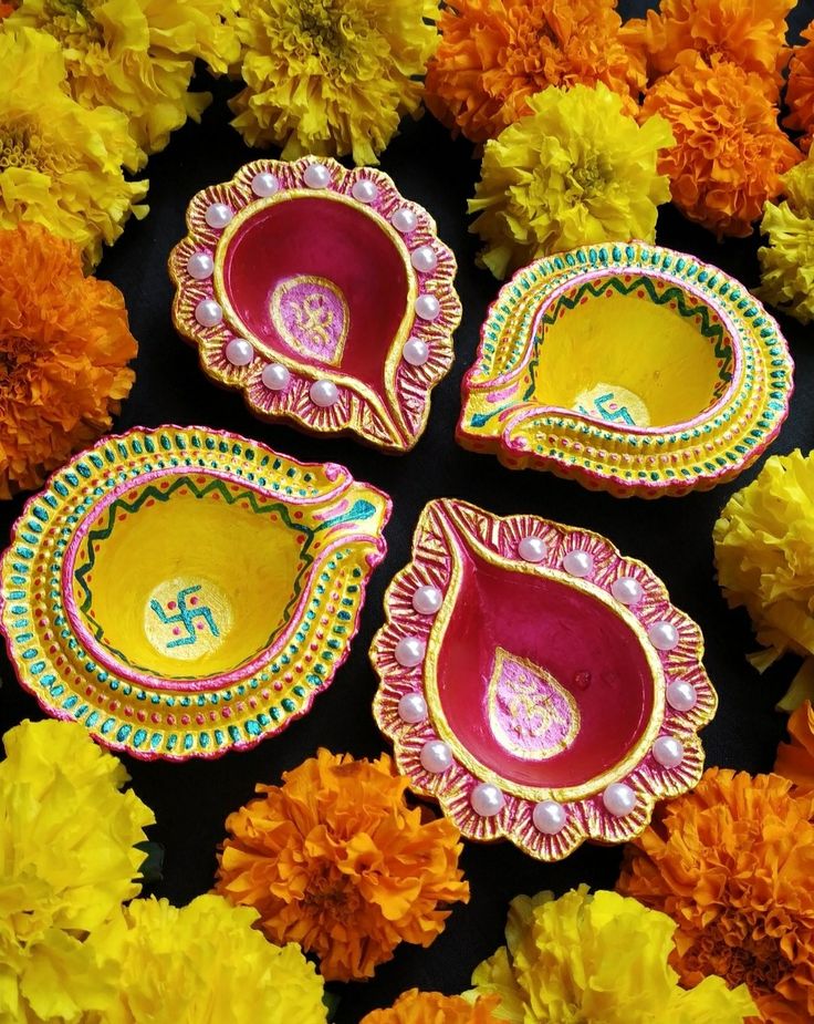 four colorfully decorated dishes sitting on top of yellow and orange flowers in front of a black background