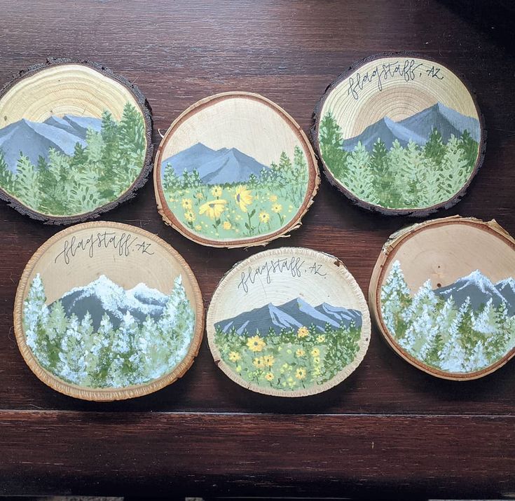 four painted wooden slices with trees and mountains on them