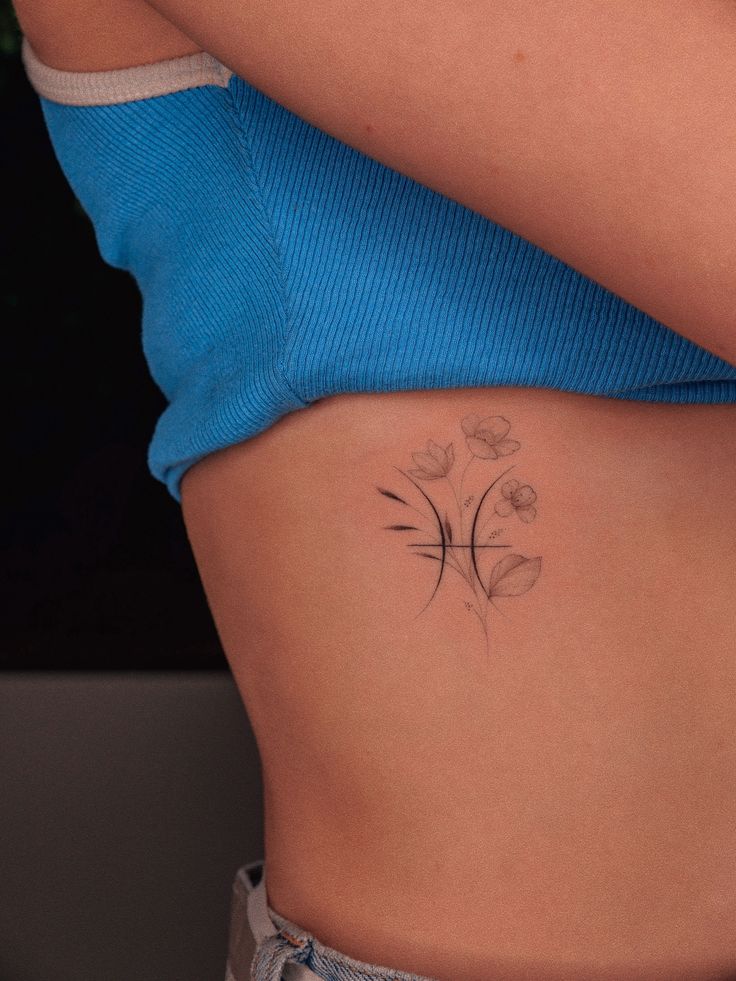 a woman's stomach with a flower tattoo on her left side ribcage