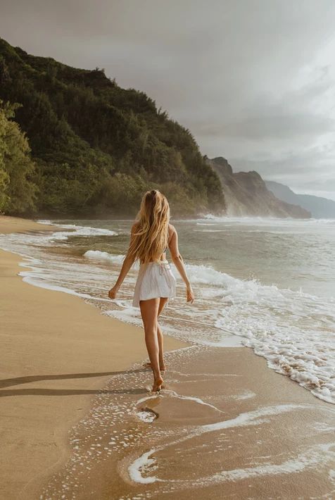 a woman walking along the beach towards the ocean