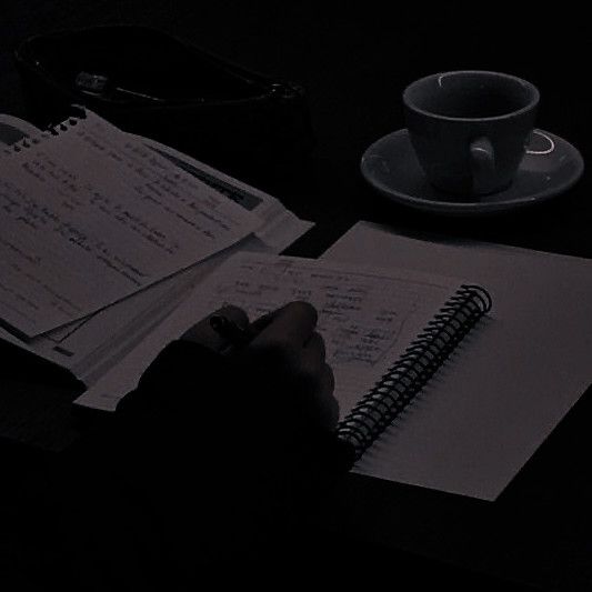 a person writing in a notebook next to a coffee cup