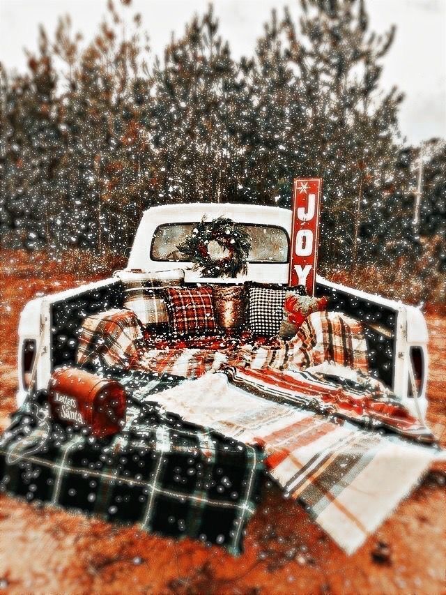 an old pickup truck is parked in the snow with plaid blankets and pillows on it