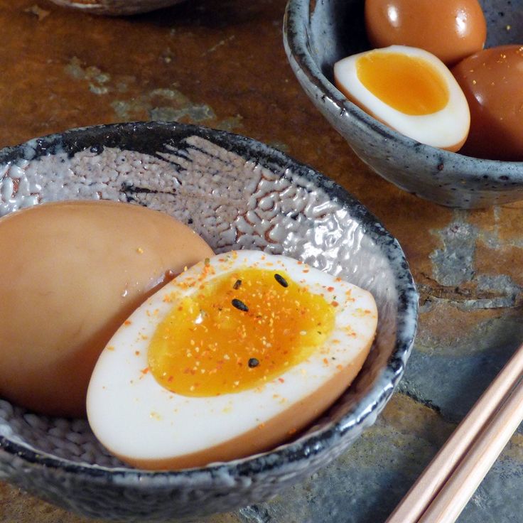 two bowls with eggs and chopsticks next to each other on a stone table