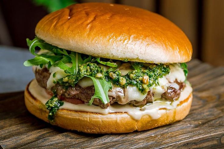 a sandwich with meat, broccoli and cheese on it sitting on a wooden table