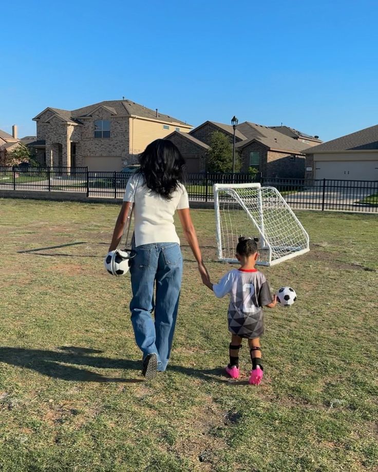 a woman holding the hand of a small child as they walk towards a soccer goal