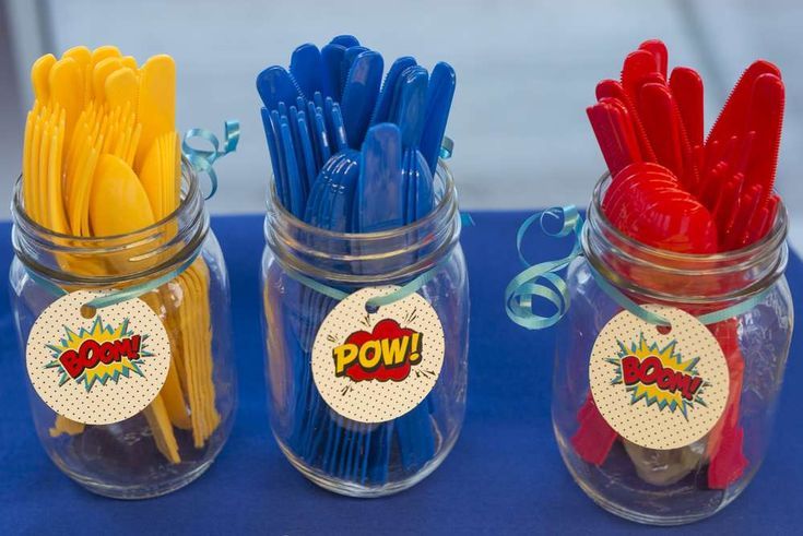 three jars filled with different colored plastic utensils on top of a blue table