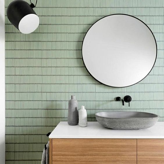 a bathroom with green tiles and a round mirror on the wall, along with a wooden cabinet