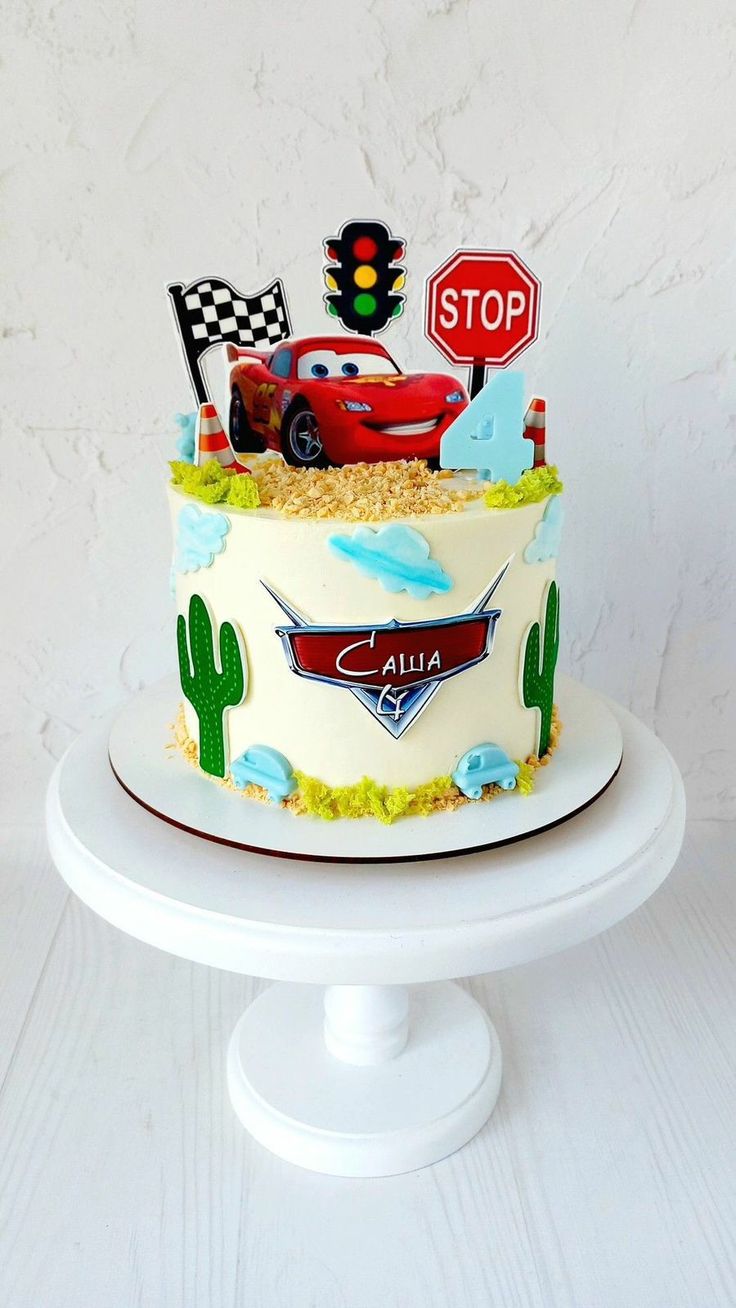 a cake with cars on it sitting on top of a white pedestal next to a stop sign