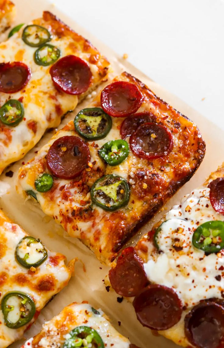 several slices of pepperoni pizza on a white platter with green peppers and jalapenos