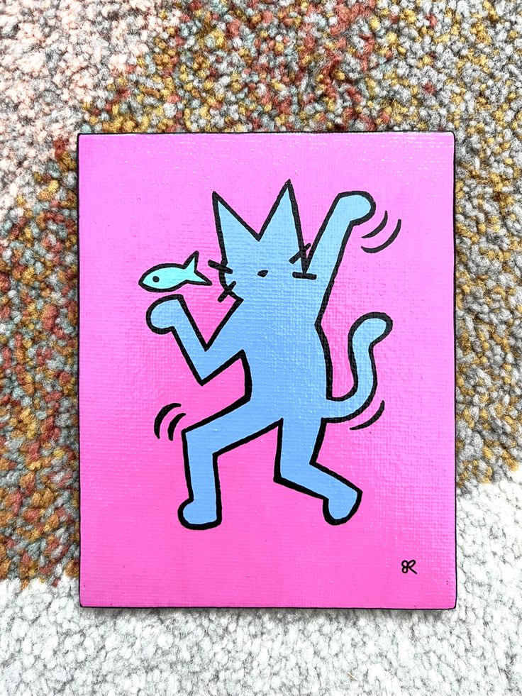 a pink and blue square with a cartoon cat on it's back side, in front of a carpeted area