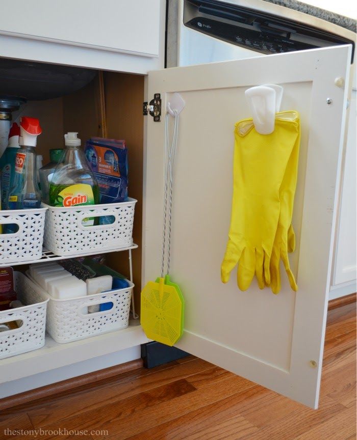 a yellow glove hanging on the door of a white cabinet with cleaning products in it